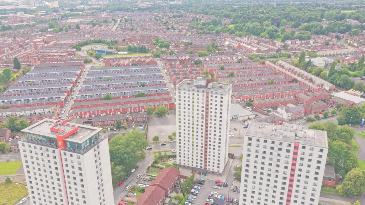High-rise residential towers in Salford, Greater Manchester, England, stand among rows of terraced houses and tree-lined streets, captured in an ascending aerial drone shot