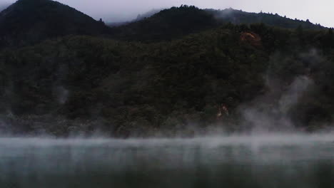 zoom out shot of steam rising over geothermal pond in volcanic region, new zealand, north island