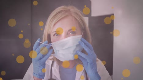 animation of yellow spots over female caucasian doctor putting face mask on