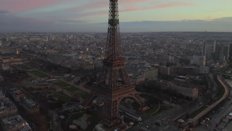 Aerial-ascending-footage-of-famous-Eiffel-Tower-and-surrounding-gardens-at-dusk.-Town-development-in-metropolis-in-background.-Paris,-France
