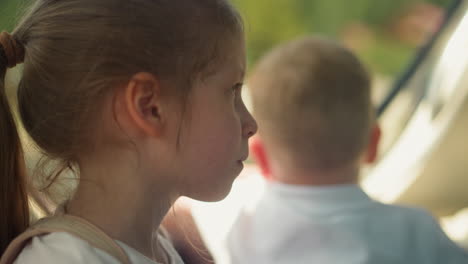 cute little girl with ponytail sits with brother near motorboat window closeup. sister turns head to look at toddler boy during river cruise