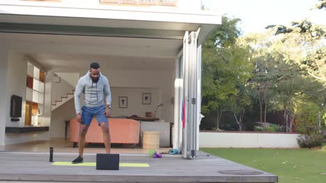 Hombre-Afroamericano-Enfocado-En-Entrenamiento-Físico-Estirándose-En-Cubierta-En-Un-Jardín-Soleado,-Cámara-Lenta