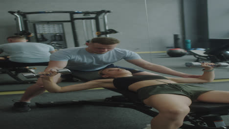 woman doing dumbbell press with fitness trainer