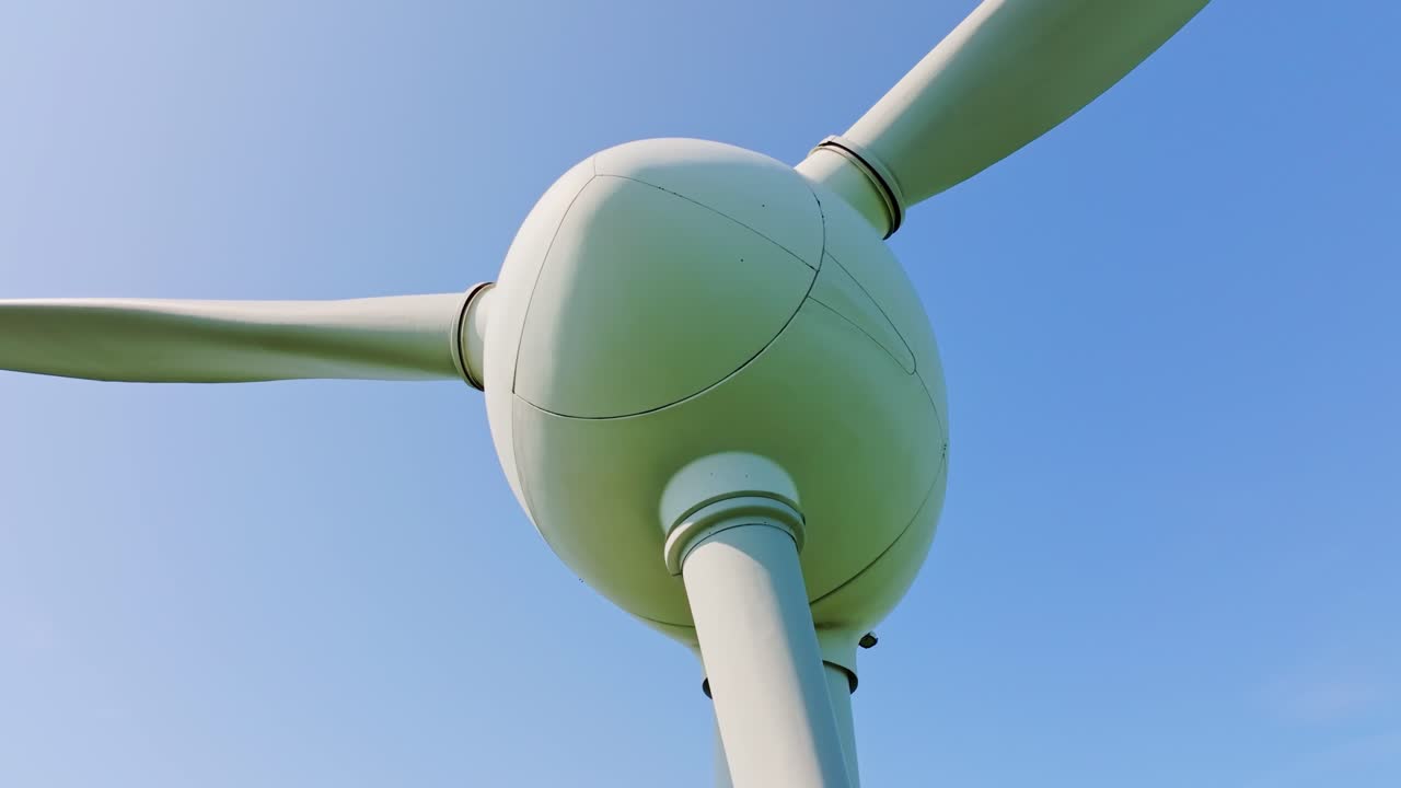 Still wind turbine under clear blue sky as drone ascends and rotates smoothly