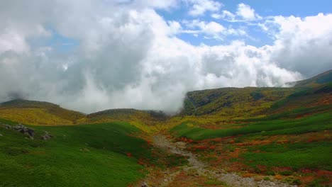 Eine-Atemberaubende-Drohnenaufnahme-Aus-Der-Vogelperspektive-Fängt-Eine-Majestätische-Bergklippe-Mit-Blick-Auf-Ein-Atemberaubendes-Tal-Voller-Wirbelnder-Wolken-Und-Leuchtend-Herbstlich-Gefärbter-Bäume-Ein
