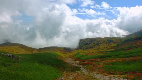 Una-Impactante-Toma-De-Un-Dron-De-ángulo-Alto-Captura-Un-Majestuoso-Acantilado-De-Montaña-Con-Vista-A-Un-Impresionante-Valle-Lleno-De-Nubes-Arremolinadas-Y-Vibrantes-árboles-De-Colores-Otoñales