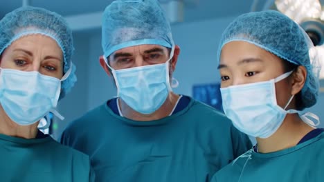 medical team analyzing patient data in surgical room: surgeons in scrubs with masks focused on monitors for critical health insights