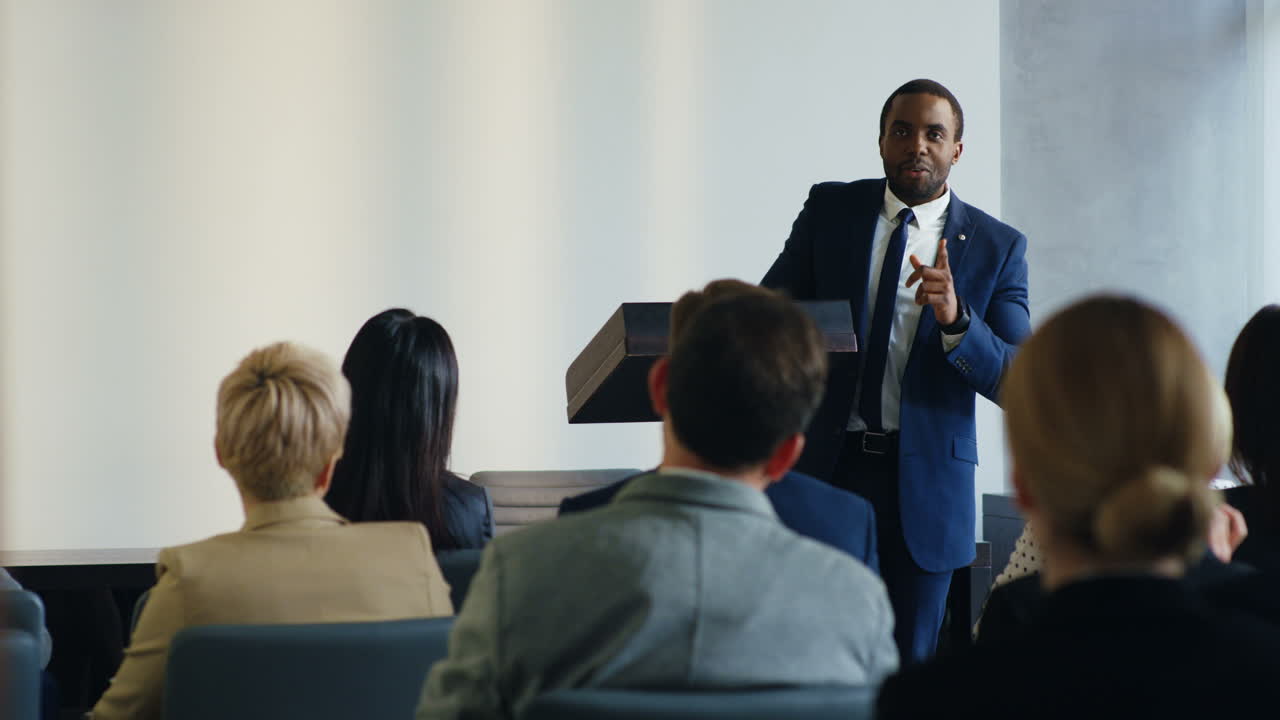 African American businessman speaker on a podium at a conference and interacting with people in the hall during his speech