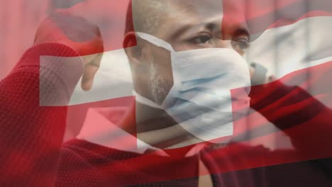 Animation-of-flag-of-switzerland-waving-over-african-american-man-wearing-face-mask-in-city-street