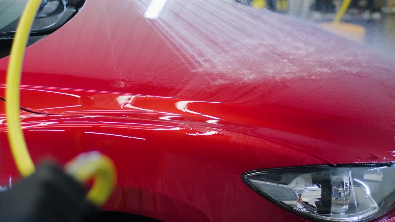 hombre trabajador lavando coche rojo en un lavado de coches.
