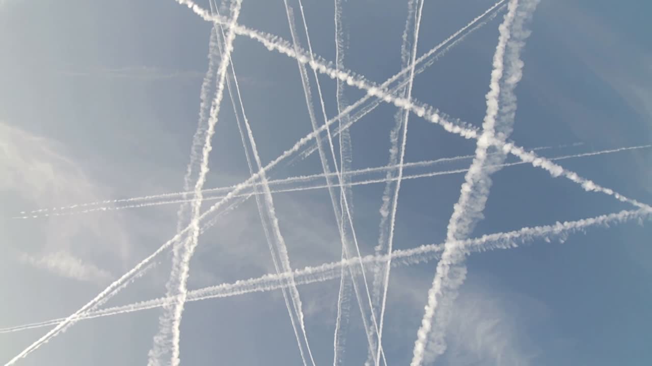 Passing jets creating crossing contrails in humid upper air over blue sky, showing thin lines