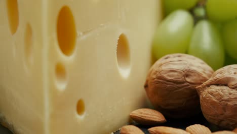 close up part of medium hard cheese head edam gouda parmesan on wooden board, with nuts and grapes rotaiting on the plate