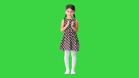 niña con vestido de puntos polca aplaudiendo sus manos mirando a la cámara en una pantalla verde, llave de croma