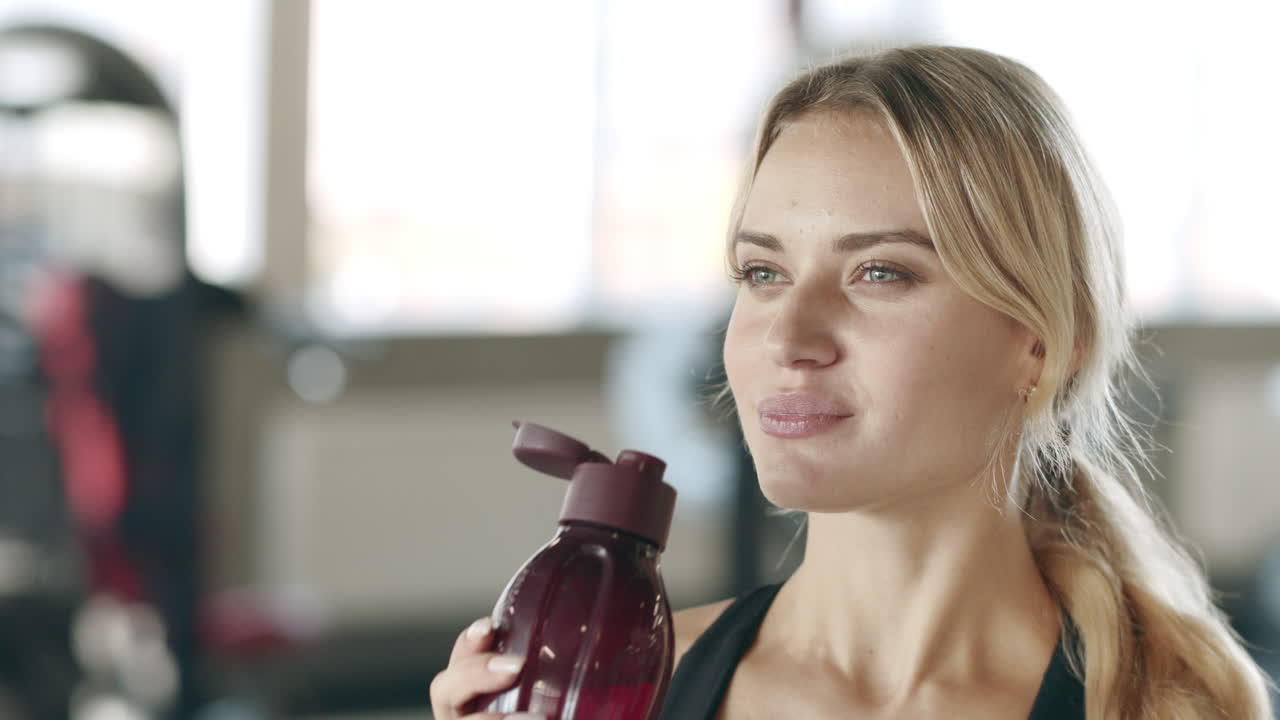 mujer sedienta disfrutando del agua después del entrenamiento de fitness en el gimnasio.
