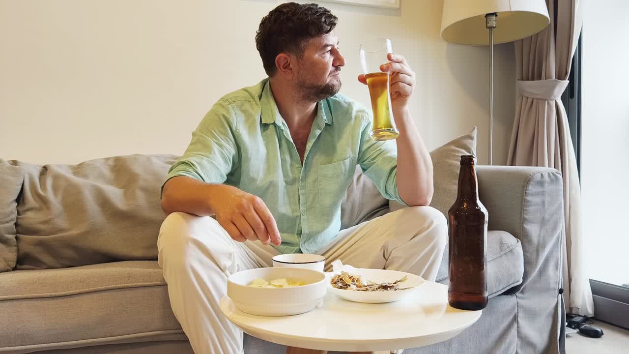 Man relaxing on a sofa, drinking beer and eating snacks