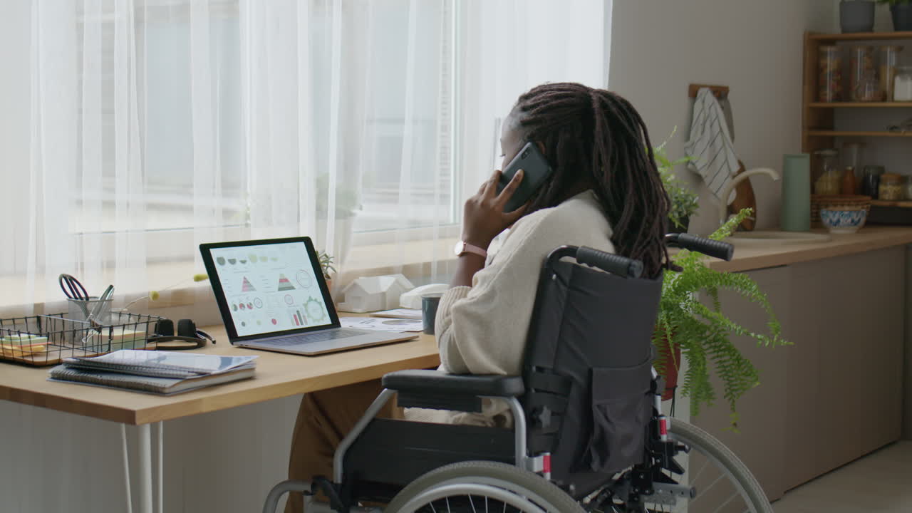Businesswoman in Wheelchair Talking on Phone and Using Laptop at Home