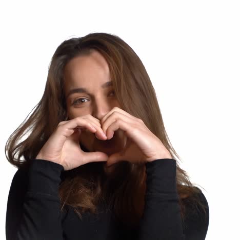 a pretty woman is showing heart by her hands ahead of herself on a white background in the studio. non-verbal communication.