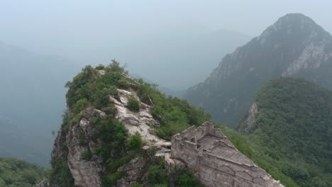 Fly-over-old-part-of-Great-Wall-of-China-with-deteriorate-lookout-tower-on-top-of-mountain-on-a-cloudy-day