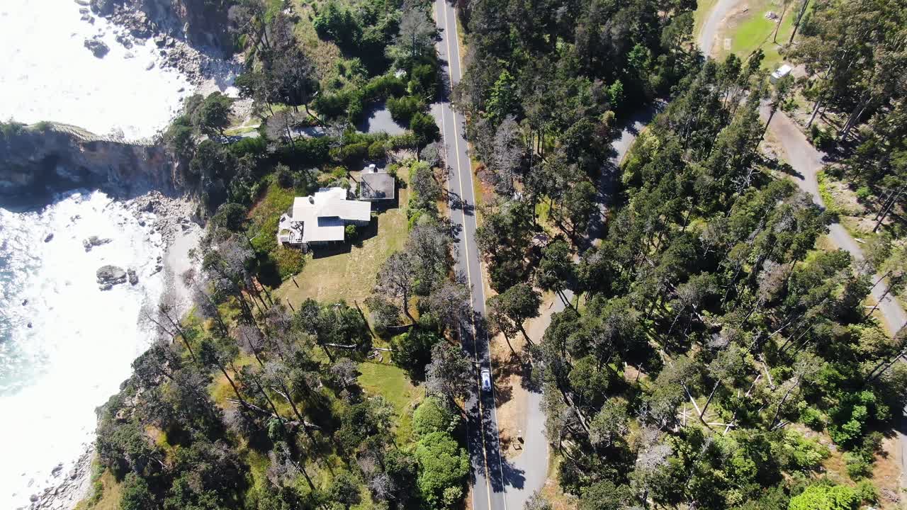 imágenes aéreas desde arriba siguiendo una furgoneta blanca mientras atraviesa una carretera rodeada de exuberante vegetación, con una orilla rocosa en el lado derecho en el bosque nacional de lassen, california