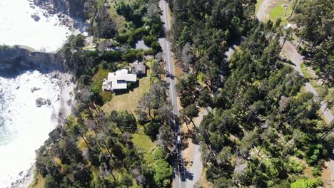 Aerial-top-view-footage-following-a-white-van-as-it-traverses-a-road-surrounded-by-lush-greenery,-with-a-rocky-shore-on-the-right-side-in-Lassen-National-Forest,-California