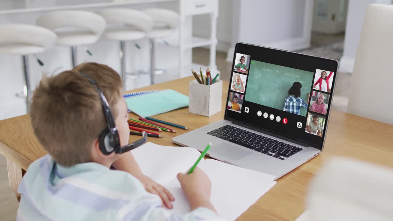 Schoolboy using laptop for online lesson at home, with diverse teacher and class on screen