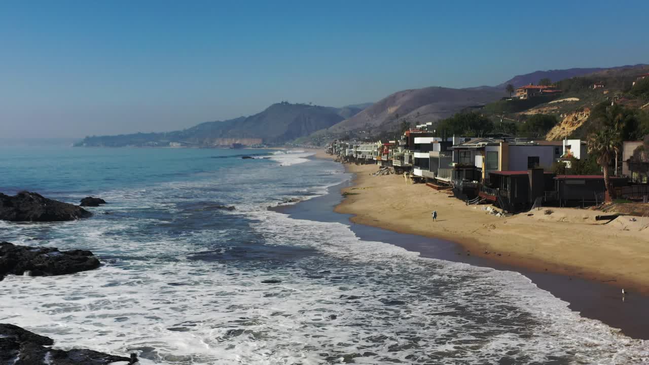 Ripresa aerea 4K con drone della costa balneare in California, con l'Oceano Pacifico blu e le onde che si infrangono, e una spiaggia con belle case sullo sfondo.
