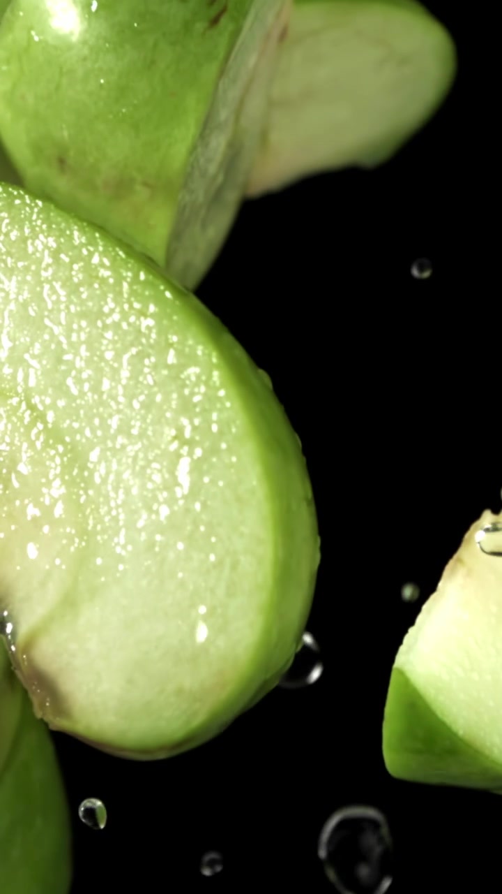 Fette di mela verde fresca che cadono con gocce d'acqua al rallentatore