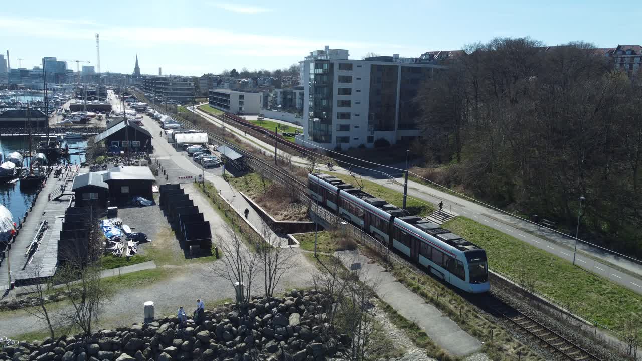 Tram-train driving along the wooden ship marina in Aarhus, Denmark