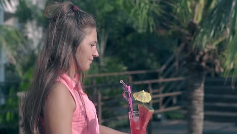 chica sostiene un cóctel rosa con sandía contra las palmas
