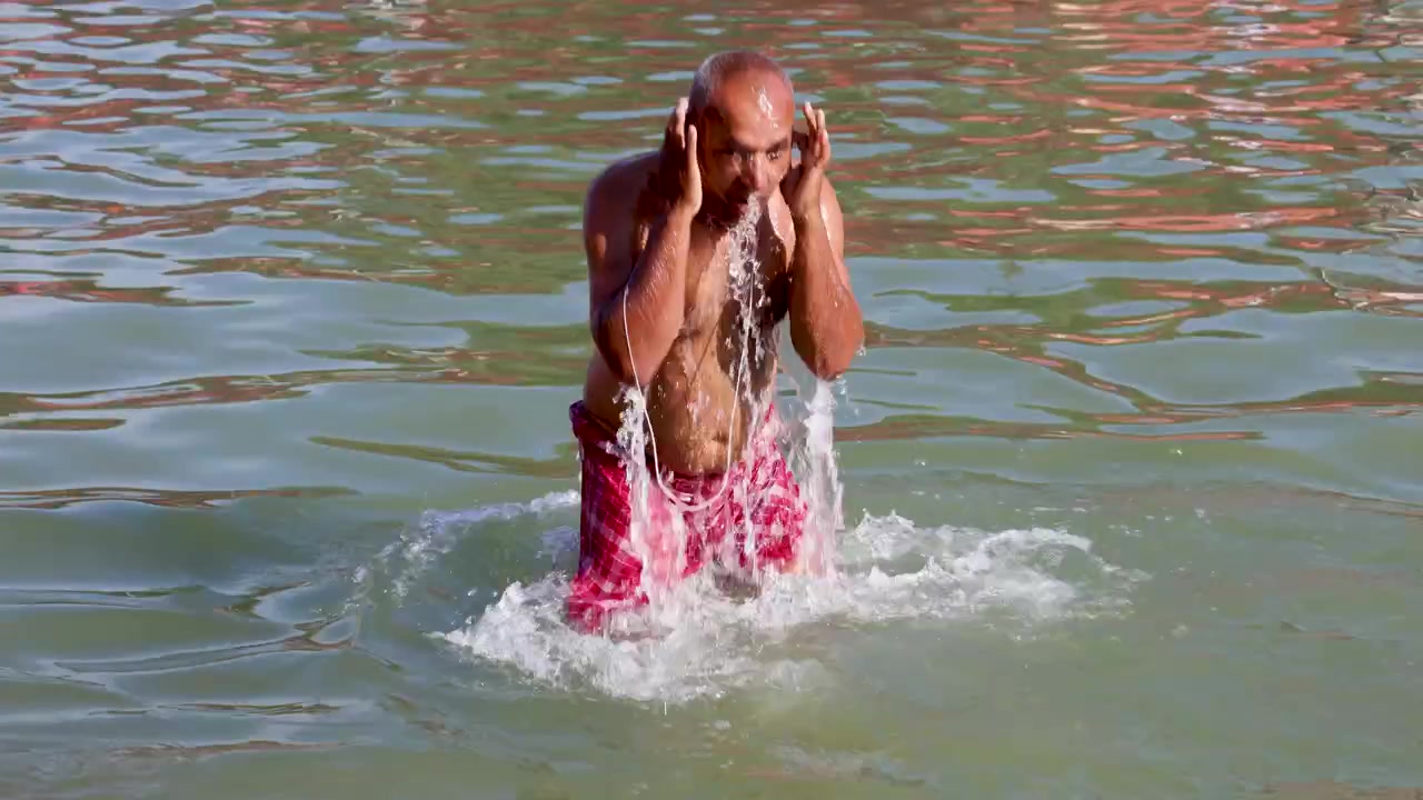 Homme effectuant un bain rituel dans l'eau d'une rivière sacrée pour une purification spirituelle