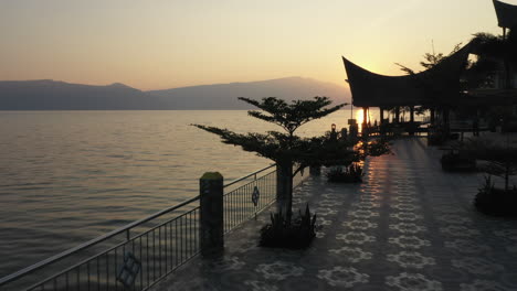 Drone-fly-through-footage-under-a-pergola-at-a-waterfront-resort-on-Lake-Toba-in-North-Sumatra,-Indonesia-at-sunrise