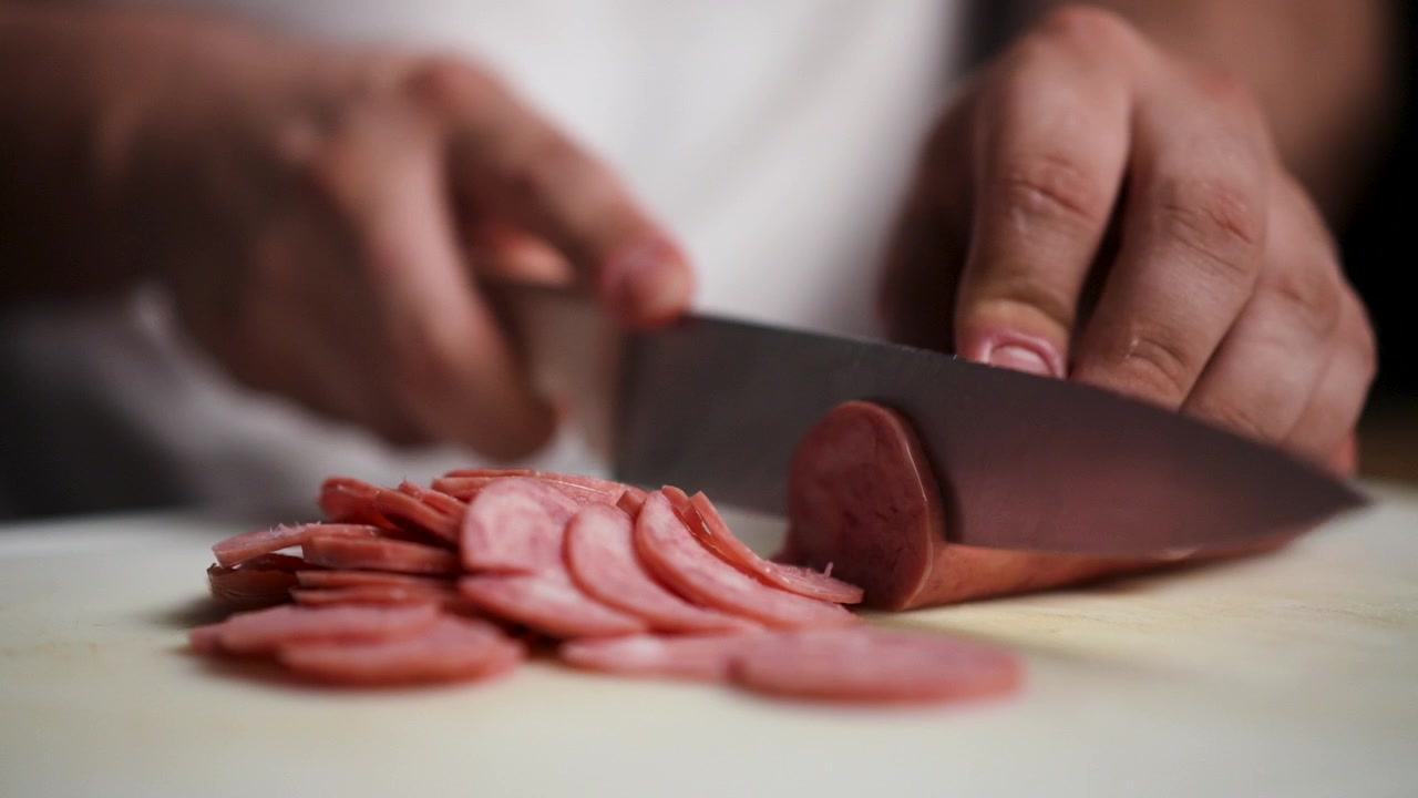 Filmato ravvicinato di uno chef che taglia il salame piccante a fette uniformi con un coltello affilato. Ideale per video sulla preparazione del cibo, tutorial di cucina o ricette