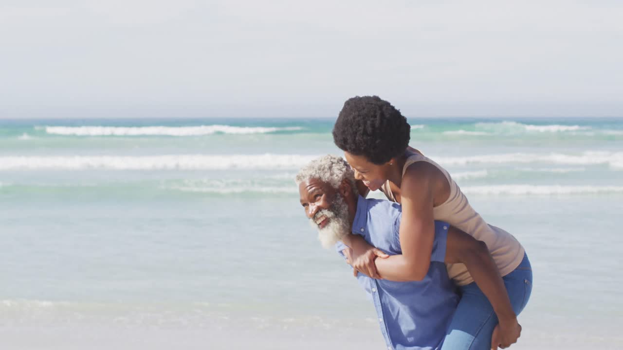 feliz pareja afroamericana caminando y abrazándose en una playa soleada