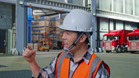 close up side view of angry asian male engineer with safety helmet shouting at someone while standing , outside of logistics distributions warehouse