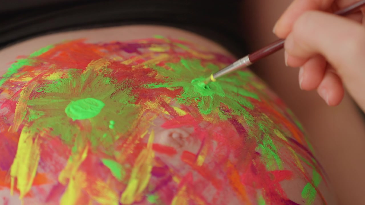 Primo piano di pancia di donna incinta dipinta con vivaci colori neon