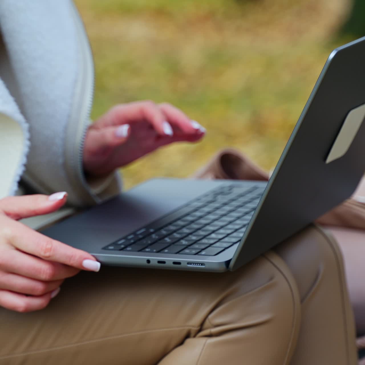 Female hands open laptop lying on the knees in beige pants. Lady sitting outdoors is going to work out of office