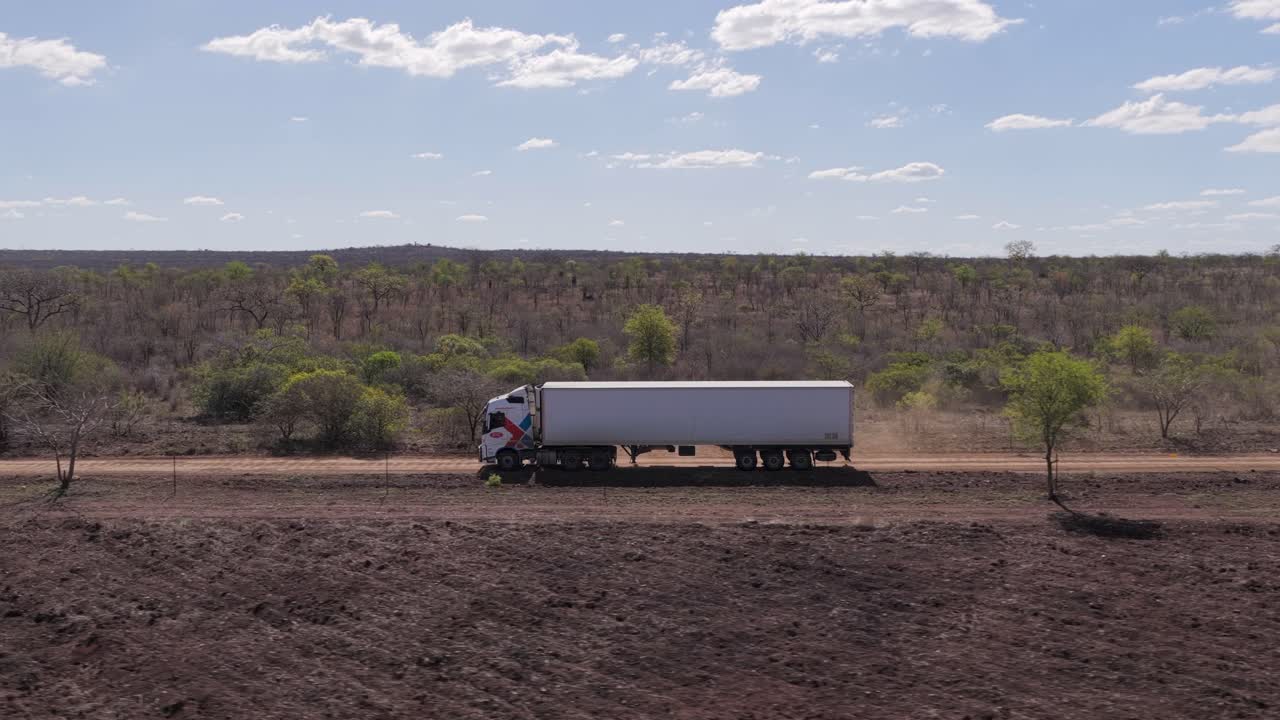 Aérea baixa ultrapassa caminhão de transporte dirigindo em estrada de terra estreita e seca