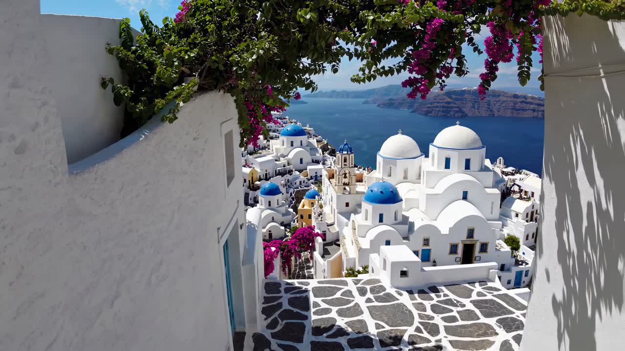 Aerial video captures iconic white and blue Santorini architecture with vibrant flowers