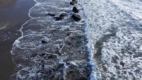 top down aerial shot of the ocean crashing against rocks in scotland