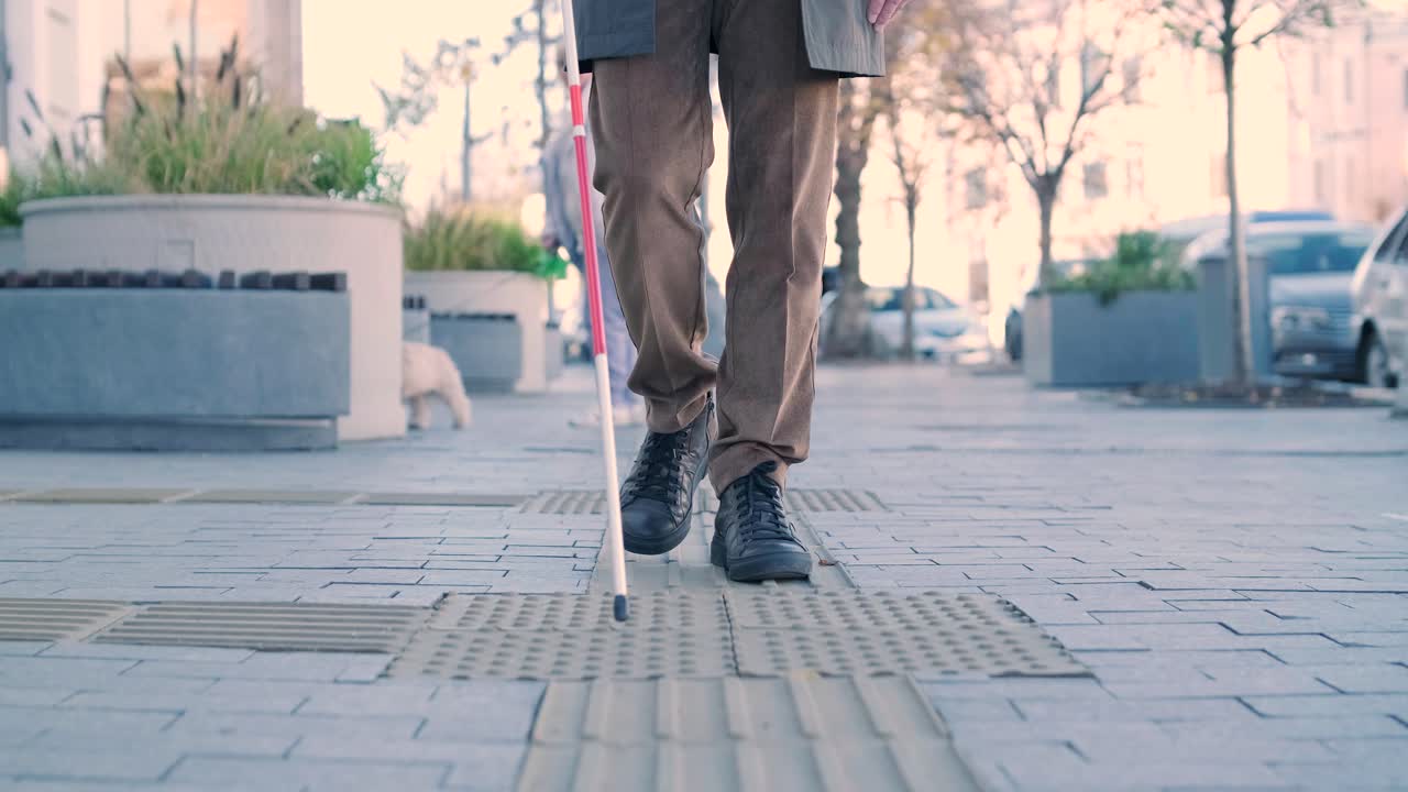Blind person using white cane on straight tactile tiles to navigate road