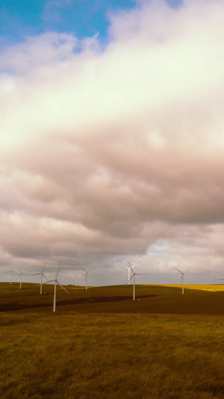 Vertical Video Wide Landscape Pan Across Dozens of Spinning Onshore Wind Turbines with Dynamic Clouds and Blue Sky. Green Energy Farm Generating Renewable Electricity in Wales, UK