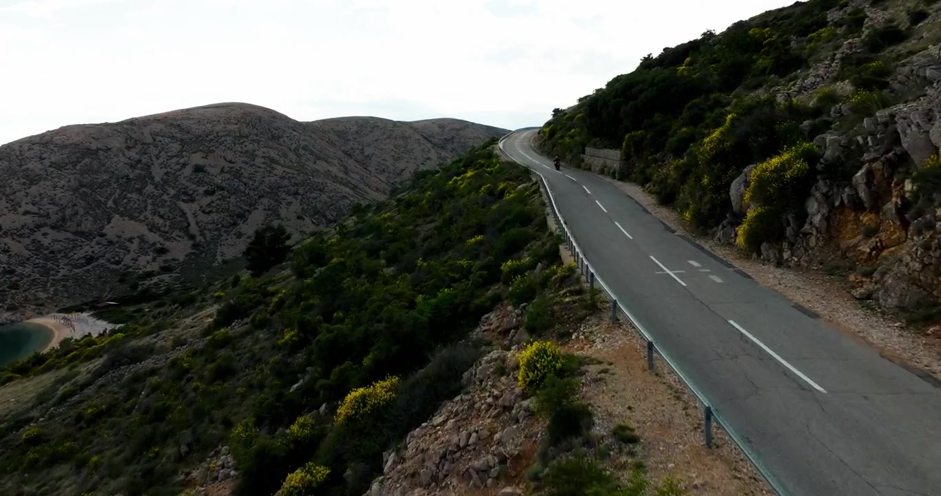 Motociclista che guida su una strada costiera vuota attraverso un paesaggio roccioso vicino al Mare Adriatico durante un'avventura di viaggio estiva.