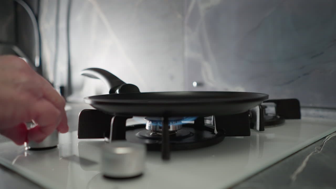 Close-up of hand turning on gas burner in modern kitchen with blue flame, preparing stove for cooking, with focus on cooking equipment, kitchen appliances, and cookware on stovetop