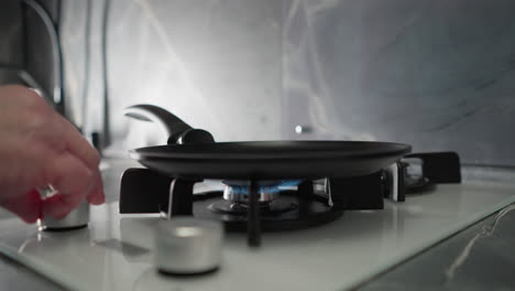 close-up of hand turning on gas burner in modern kitchen with blue flame, preparing stove for cooking, with focus on cooking equipment, kitchen appliances, and cookware on stovetop