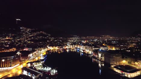 aerial dolly forward over city fjord towards bright night lights in bergen - norway