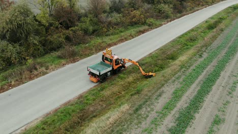 cortador cortando el césped en el hombro de la carretera con el brazo de cortar el borde
