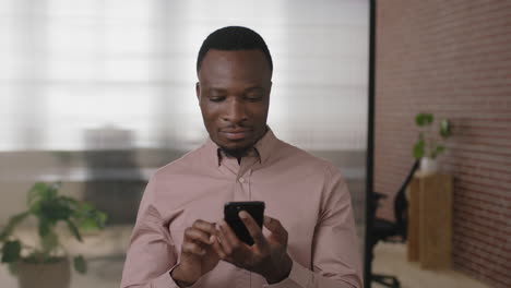 portrait of young african american businessman texting browsing using smartphone networking app in modern office workspace