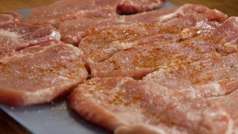 verter especias rojas sobre filetes de carne de cerdo cruda en vista de cerca
