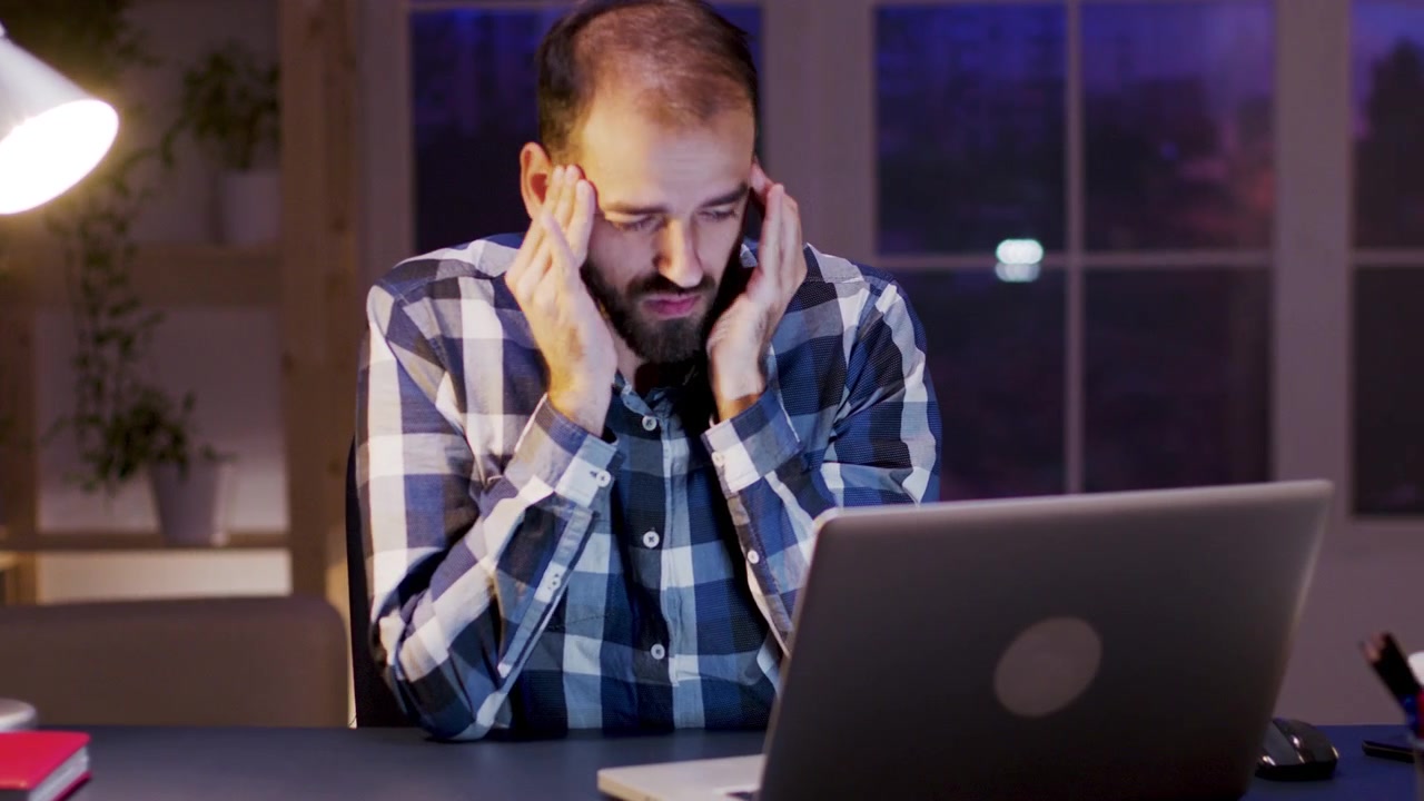 Stressed Man Working Late on Laptop in Office