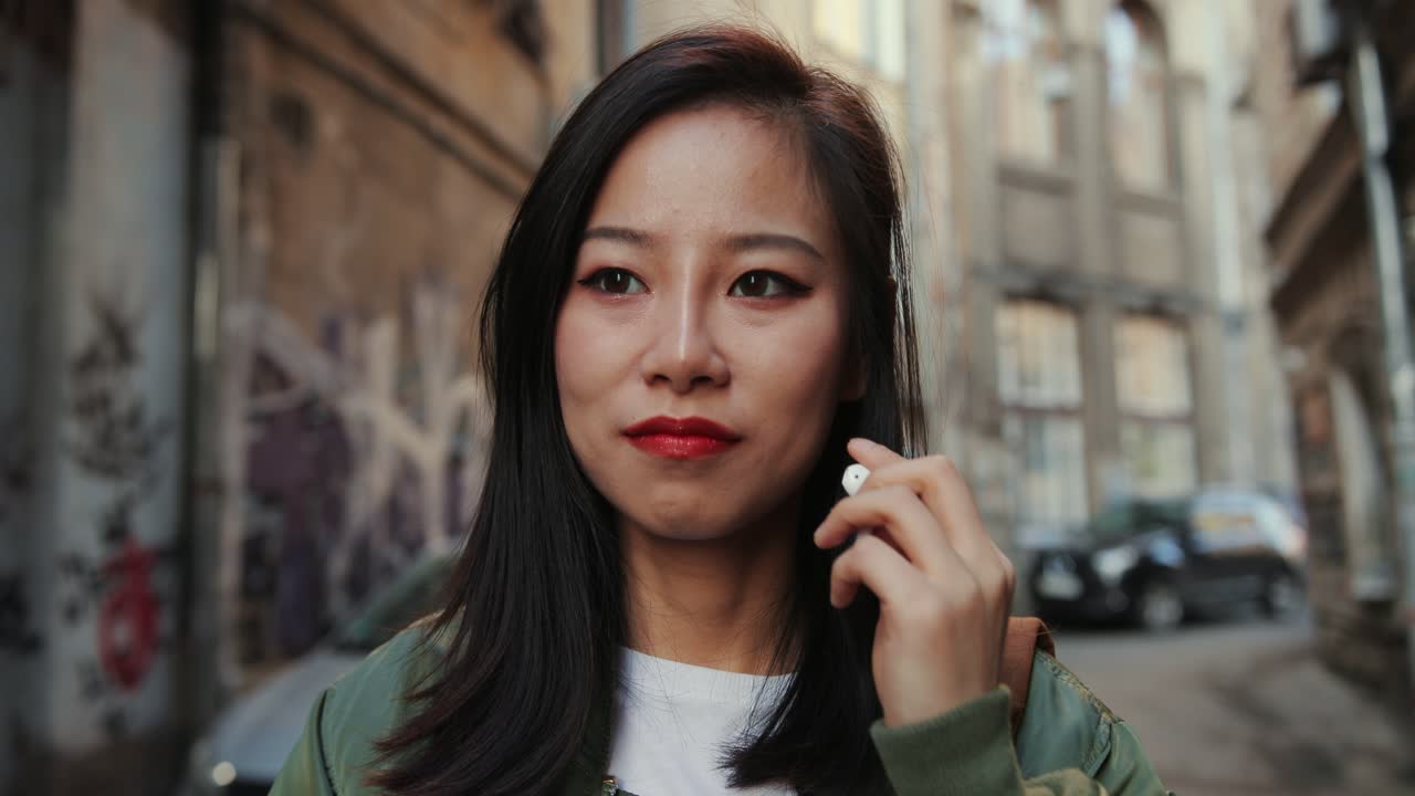 빈민가의 좁은 거리를 걷고 있는 젊고 아름다운 세련된 소녀를 가까이서 귀에 헤드폰을 끼고 즐겁게 음악을 들으며